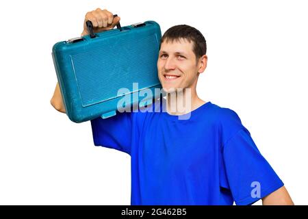 Un jeune travailleur en T-shirt bleu tient une valise avec des outils sur son épaule et sourit. Portrait isolé sur fond blanc. Réparations urgentes sur appel. Banque D'Images