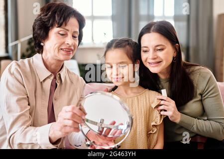 Deux femmes et petite fille mignonne regardant dans le miroir tout en appliquant le maquillage Banque D'Images