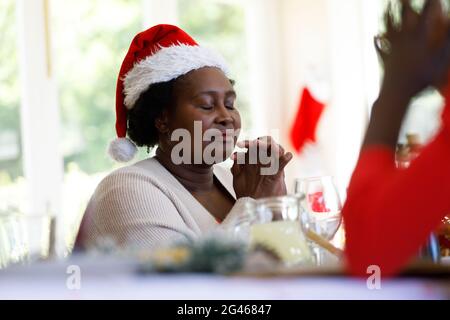 Femme afro-américaine senior assise à table et priant avant le dîner Banque D'Images