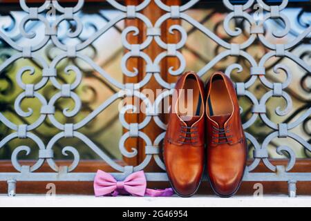 Nouvelles chaussures brunes pour hommes et noeud papillon avec ruban non attaché sur la fenêtre à l'extérieur de la grille métallique. Banque D'Images