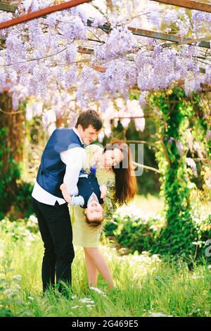 Maman et papa jouent avec leur enfant sous un arbre de wysteria Banque D'Images