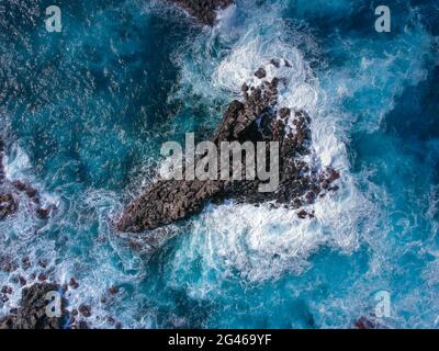 Vue aérienne du dessus des vagues de mer frappant des roches volcaniques noires sur la côte avec l'eau de mer turquoise Banque D'Images