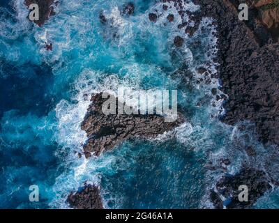 Vue aérienne du dessus des vagues de mer frappant des roches volcaniques noires sur la côte avec l'eau de mer turquoise Banque D'Images