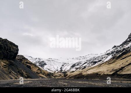 La gorge de la montagne est couverte de neige, d'herbe jaune sèche dans les contreforts de la montagne en Islande. Banque D'Images