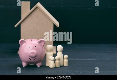 Figurines de famille en bois, banque de porc rose en céramique et maison modèle. Achat immobilier, concept de location. Déménagement dans de nouveaux appartements Banque D'Images