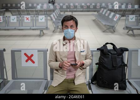 En attente d'un vol à l'aéroport vide de Chypre. Homme assis sur une chaise avec un marqueur de distance sociale au terminal vide de Paphos. Vol Banque D'Images