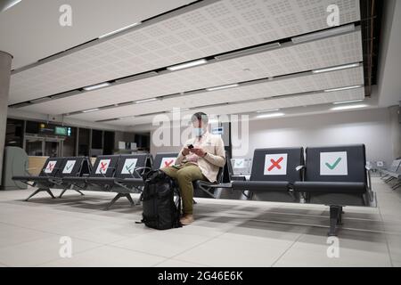 Un homme portant un masque de protection contrarié par un vol d'annulation, écrit un message à sa famille, assis dans un terminal vide à l'aéroport de Banque D'Images