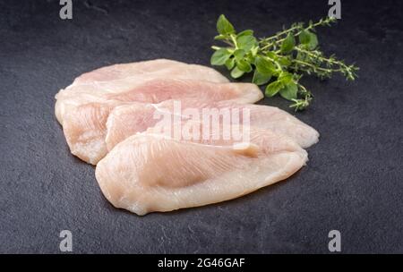 Filets d'escalope de poulet cru avec herbes offertes comme gros plan sur un tableau noir avec espace de copie Banque D'Images