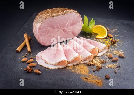 Jambon de Noël traditionnel allemand de style moderne aux épices exotiques et à l'orange offert en gros plan sur un tableau noir Banque D'Images