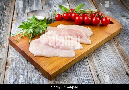 Escalope de poulet cru traditionnel avec tomates et herbes offertes en gros plan sur un plan moderne en bois avec espace de copie Banque D'Images