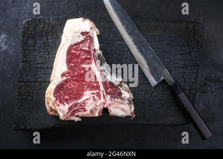 Steak de bœuf Wagyu vieilli et sec, servi en vue de dessus sur un panneau rustique en bois charré avec un couteau japonais