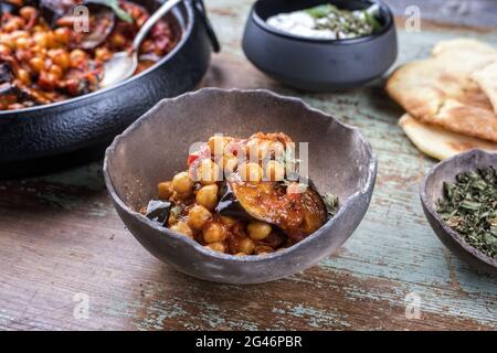 Maghmour d'aubergines libanaises cuites lentement et de style moderne, servi avec des pois chiches et du pain pita dans un cadre rustique Banque D'Images