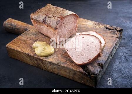 Traditionnelle leberkaese bavaroise fraîche au four, coupée en tranches et servie sous forme de morceau de moutarde épicée sur un panneau rustique en bois Banque D'Images