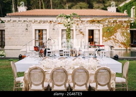 Réception de table de dîner de mariage. Tables élégantes pour les clients avec des nappes crème à motifs, sur pelouse verte, avec guirlandes et Banque D'Images