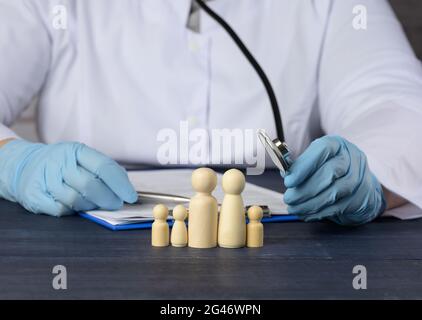 Un médecin en manteau blanc est assis à une table et à un certain nombre de figures en bois d'une famille Banque D'Images