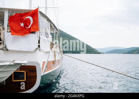 Drapeau turc sur un yacht naviguant sur une eau calme sur fond de montagnes. Banque D'Images