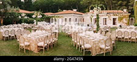 Réception de table de dîner de mariage. Tables élégantes pour les clients avec des nappes crème à motifs, sur pelouse verte, avec guirlandes et Banque D'Images