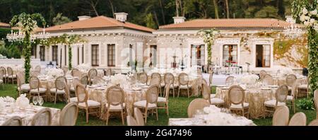 Réception de table de dîner de mariage. Tables élégantes pour les clients avec des nappes crème à motifs, sur pelouse verte, avec guirlandes et Banque D'Images