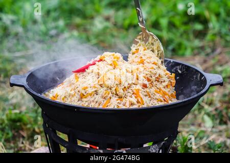 Cuisson du riz pilaf dans un grand pot en fonte au feu Banque D'Images