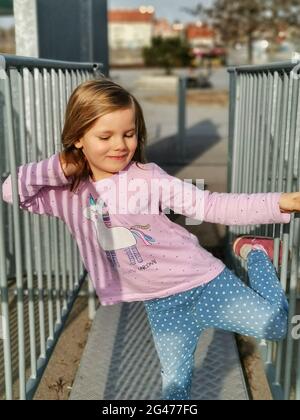 Tir vertical de la petite fille blonde caucasienne dansant et posant avec ses yeux fermés. Banque D'Images