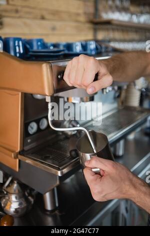 Gros plan des mains du serveur versant du lait dans le pot de la machine à café Banque D'Images