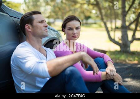 Un couple fatigué assis à côté d'une voiture de dépannage Banque D'Images