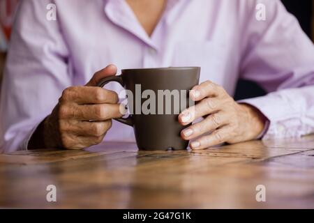 Section médiane de la femme tenant le mug tout en étant assis à la table Banque D'Images