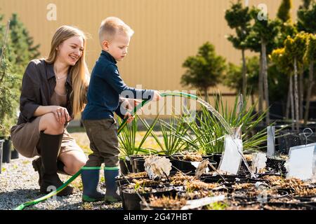 Une jardinière féminine et son fils arrosoir les plantes dans des pots avec un tuyau Banque D'Images