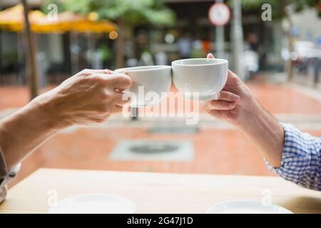 Mains d'un couple senior qui toasque des tasses à café Banque D'Images