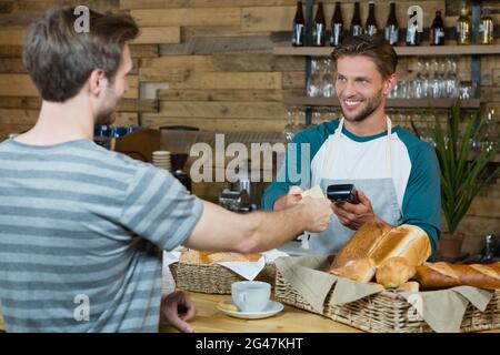 Serveur souriant recevant la carte de crédit du client pour le paiement au comptoir Banque D'Images