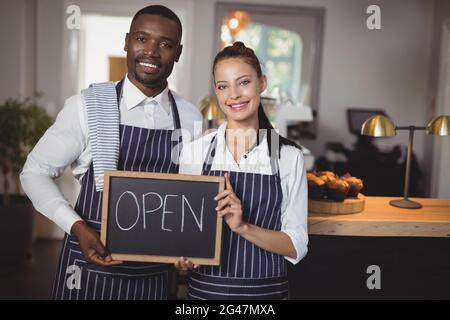 Un serveur et une serveuse souriants montrant un tableau noir avec une enseigne ouverte Banque D'Images