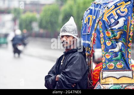 Dhaka, Bangladesh. 19 juin 2021. Un extracteur de pousse-pousse debout à côté de la route attend des passagers lors d'une pluie à Dhaka. La forte baisse de la mousson a causé une exploitation forestière extrême dans la plupart des régions de la ville de Dhaka, au Bangladesh. Les routes ont été submergées, ce qui a rendu les déplacements lents et dangereux. Crédit : SOPA Images Limited/Alamy Live News Banque D'Images