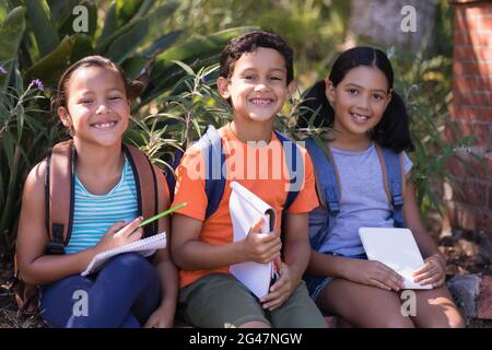 Des amis souriants avec des livres et des tablettes numériques assis sur un mur de soutènement Banque D'Images