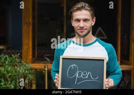 Portrait of smiling waiter holding chalkboard with open sign Banque D'Images
