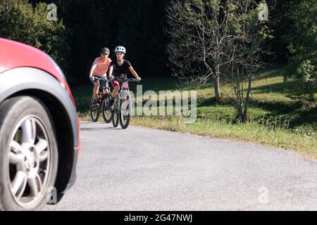 Voiture et deux cyclistes féminins en danger sur une route de circulation avec la voiture qui se dirige vers eux. Banque D'Images
