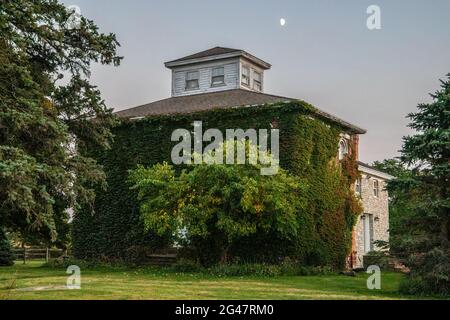 Ancienne ferme en briques recouverte de vignes avec une coupole sur le dessus sous la lune. Banque D'Images