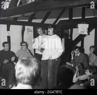 1970, historique, concert de pub, musique folklorique, dans un pub de campagne avec poutres en bois, un pull d'homme et tenant une pinte de bière chantant une chanson, Essex, Angleterre, Royaume-Uni. Banque D'Images