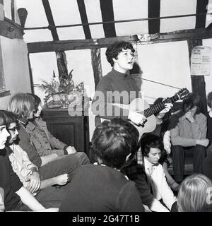 1970, musique folklorique historique, dans une salle d'un pub de campagne avec poutres en bois, un public écoutant une jeune chanteuse folklorique jouant une guitare et chantant une chanson au Castle Inn, Colchester, Essex, Angleterre, Royaume-Uni. Banque D'Images