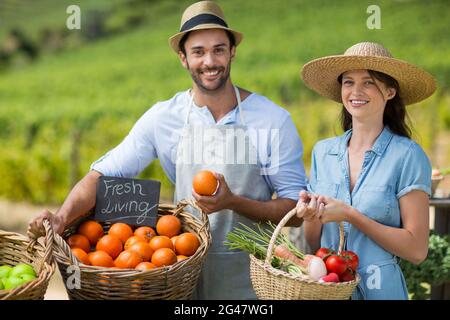 Homme et femme souriants debout près de légumes frais au marché fermier Banque D'Images