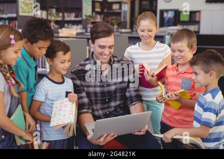 Enseignant et écoliers utilisant un ordinateur portable dans la bibliothèque Banque D'Images