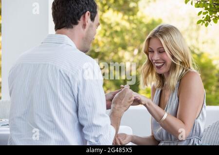 Homme mettant l'anneau sur le doigt de la femme au restaurant Banque D'Images