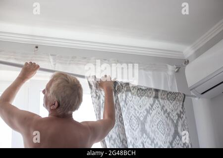 Un homme adulte porte un rideau sur la fenêtre. Travaux ménagers et nouvelle rénovation. Banque D'Images