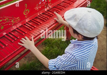 Garçon dans un béret beige joue le piano rouge à l'extérieur lors d'une belle journée ensoleillée d'été Banque D'Images