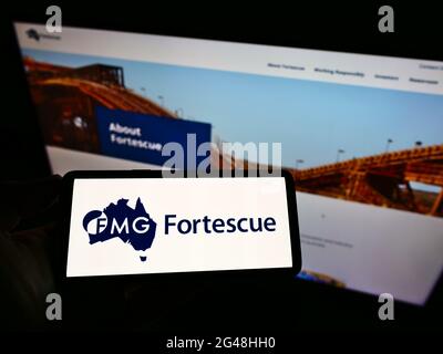 Personne tenant un téléphone portable avec le logo de la société minière australienne Fortescue Metals Group Ltd à l'écran devant la page Web. Mise au point sur l'affichage du téléphone. Banque D'Images