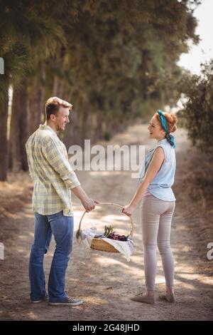 Jeune couple joyeux portant le panier sur la route de terre à la ferme Banque D'Images