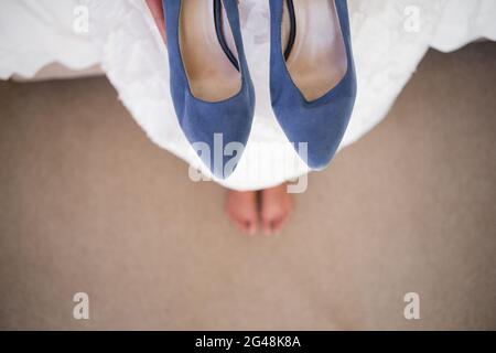 Section basse de la mariée tenant des chaussures bleues tout en étant assis dans les cabines d'essayage Banque D'Images