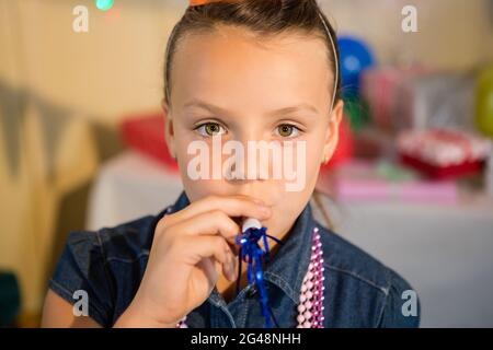 Jeune fille soufflant corne de fête pendant la fête d'anniversaire Banque D'Images