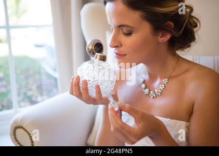 Belle mariée sentant le parfum tout en étant assis sur un fauteuil Banque D'Images