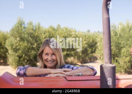 Portrait d'une femme heureuse penchée sur un tracteur dans une oliveraie Banque D'Images