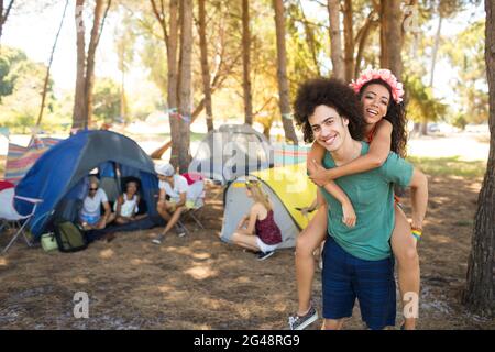 Joyeux jeune homme piggysoutenant la femme avec des amis en arrière-plan Banque D'Images